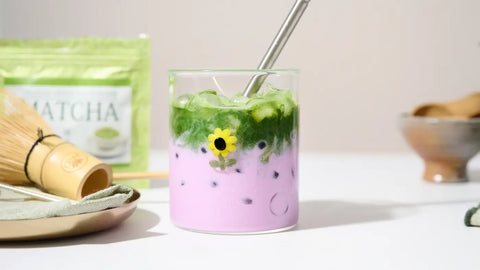 ube matcha latte with two-layered of matcha tea and purple ube in a glass with a straw on a textured surface.